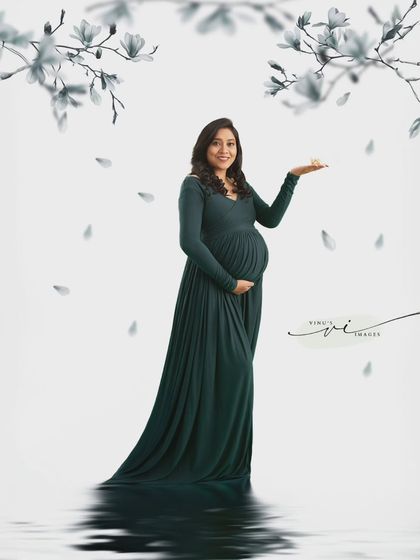 A creative composition with falling white petals. The mother-to-be stands in her green gown, reflected in the water below, creating a serene and artistic portrait.