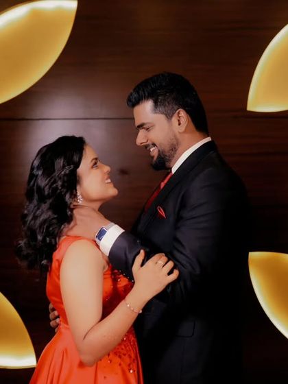 A couple shares a loving gaze in a stylishly lit room. The warm, leaf-shaped wall lights create a modern and intimate backdrop for this portrait.