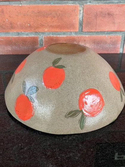 A large, round bowl hand-painted with bright oranges. This cheerful piece is perfect as a fruit bowl or a statement serving dish.
