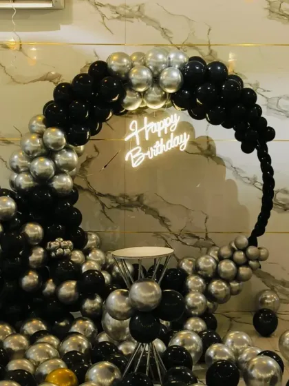 A sleek and modern black and chrome silver balloon ring. This minimalist yet impactful design is perfect for a sophisticated adult birthday party, with a neon sign and a cake pedestal in the center.