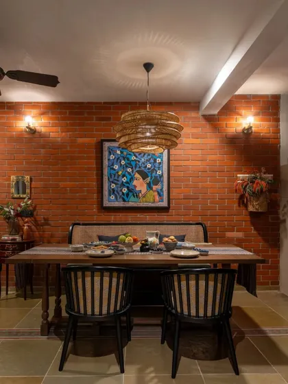 In this Dhaka home, the dining area is set against a warm, exposed brick wall. A large painting adds a vibrant splash of color, while the wicker pendant light brings a touch of natural texture. It’s a space designed for enjoying meals with family and friends.
