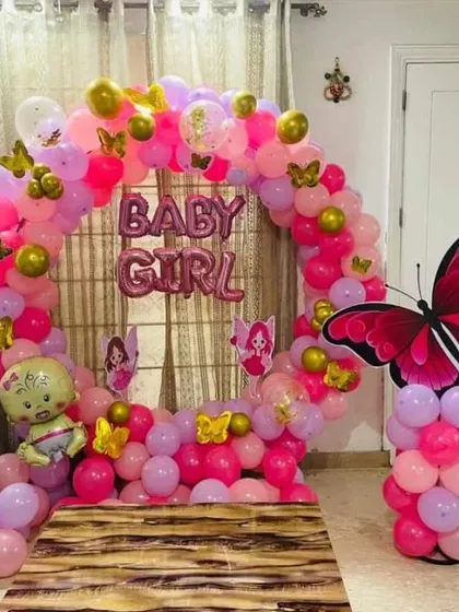 A 'Baby Girl' welcome decoration with a circular balloon arch in shades of pink and gold.