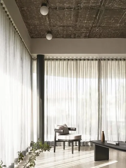 Light filters through sheer curtains in the living room of Pavilion House. The design uses expansive glass and a textured, exposed concrete ceiling to create a space that feels both open to the elements and securely sheltered.