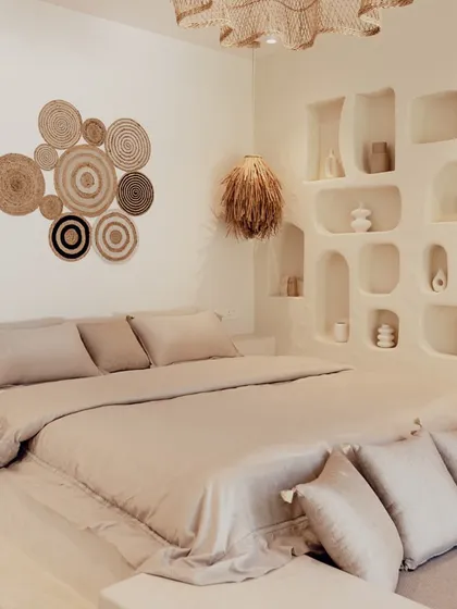 This serene bedroom is a perfect example of a 'Goodu'. I used a monolithic, lime-washed platform for the bed and seating, complemented by natural fiber wall art and light fixtures to create a space that feels grounded and peaceful.
