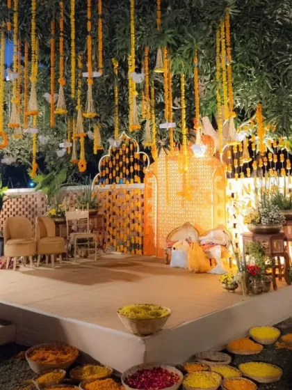 An evening Haldi stage setup. The decor features hanging marigold garlands and a beautifully lit backdrop, creating a warm and inviting atmosphere for the night's rituals.