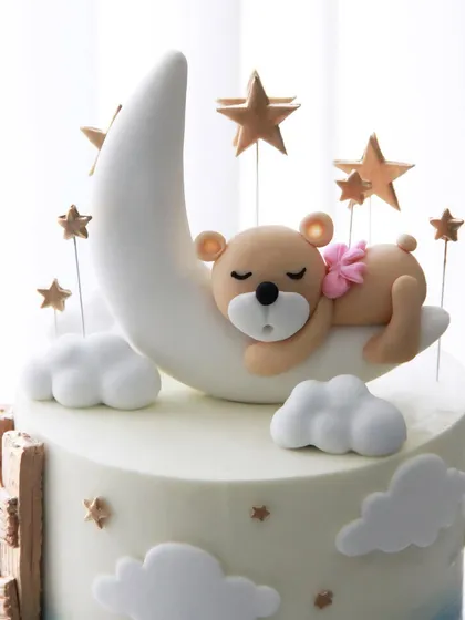 The sweet teddy bear topper, sleeping peacefully on a crescent moon among the stars.