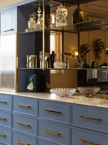 A close-up of the custom-designed crockery unit, featuring a tinted mirror back, glass shelves, and a beautiful dusty blue finish.