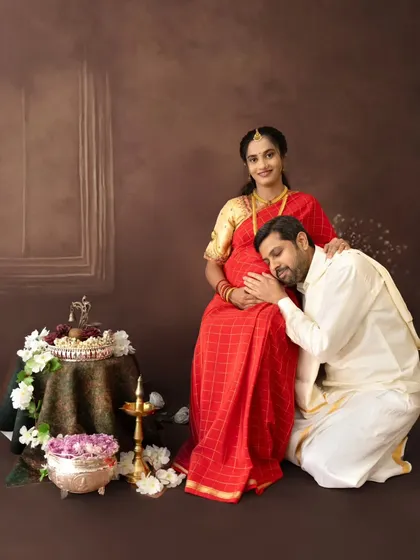 A tender moment during a traditional maternity photoshoot. The husband-to-be listens to the baby bump, set against a classic, painterly backdrop, blending cultural elegance with heartfelt emotion.