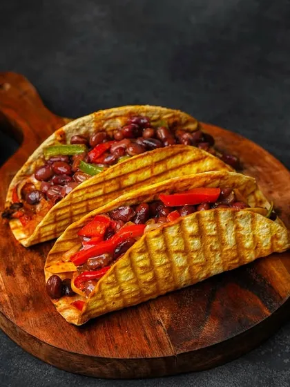 A wider shot of the bean tacos on a wooden board, showing more of the dark, textured background. This gives the image a sense of place and atmosphere.