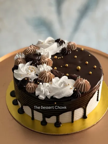 A beautiful chocolate drip cake with a mix of chocolate and vanilla cream swirls on top.