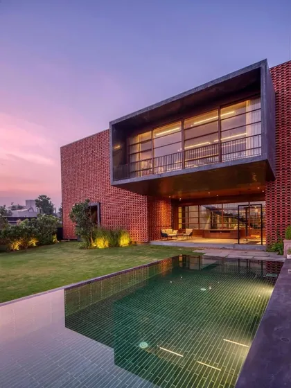 As dusk settles, the homes we design take on a new life. Here, the warm glow from the interior reflects on the pool, while the landscape lighting begins to highlight the textures of the brick facade and the surrounding greenery, creating a tranquil evening ambiance.