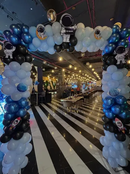 A grand entrance arch for a Space-themed party, with columns of blue, black, and white balloons and astronaut cutouts.