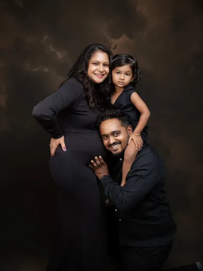 A portrait of pure family joy. Dad listens to the baby bump while big sister gets a piggyback ride. It's a moment of fun, love, and connection, beautifully captured in a classic studio setting.