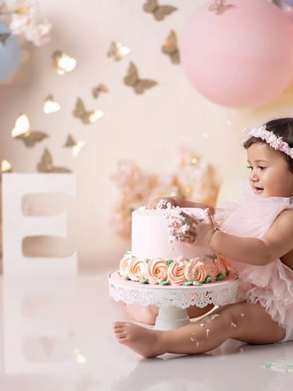 This little angel is ready to dig into her cake. The pastel balloons and butterfly decorations create a whimsical scene.