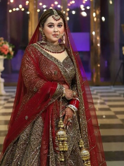 A stunning bride in a deep red, heavily embroidered lehenga. The makeup is bold and glamorous to match the grandeur of her outfit.