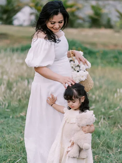 A mother and daughter moment during a maternity session. The little girl holds her teddy bear while her mom gently strokes her hair, a sweet interaction between them before the new baby arrives.