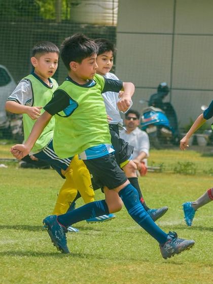 A pack of young players in green training bibs eagerly chase the ball, learning about teamwork and positioning.