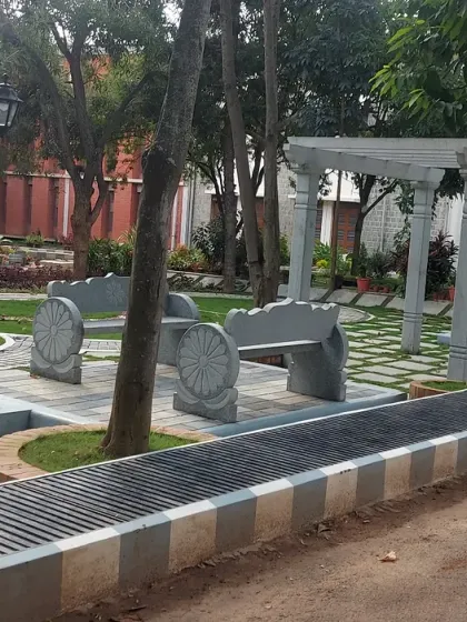 A public park area with custom stone benches, a pergola, and paved walkways. The design provides a comfortable and beautiful space for the community to gather.