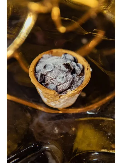 A mini ice cream cone filled with chocolate chips, presented in an elegant, frosty display. A fun and nostalgic treat for guests of all ages.