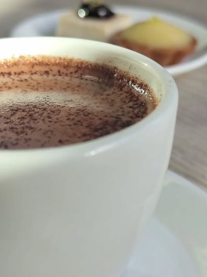 A comforting cup of hot chocolate, with delicious mini pastries like a lemon tartlet and blueberry cheesecake in the background. The perfect treat for a chilly day.