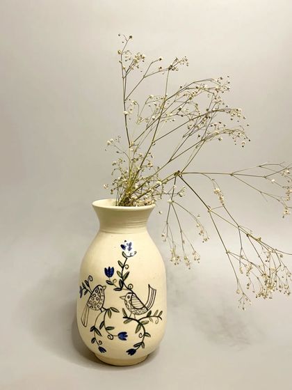 This sold vase, featuring a delicate bird and flower painting, is a testament to the artistry of handmade ceramics. Each vase is a unique piece, perfect for adding elegance to any space.