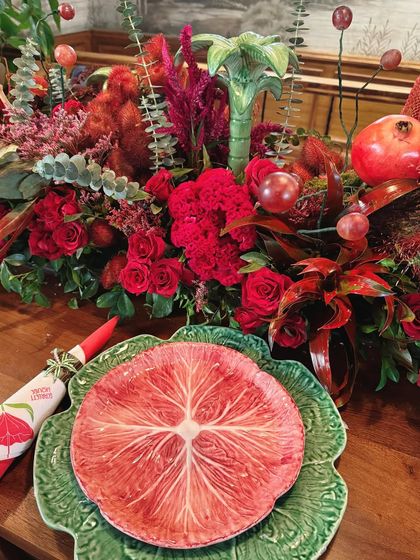 A close-up of a place setting at the Scarlett House preview, featuring unique, artistic plates and a vibrant red floral centerpiece.
