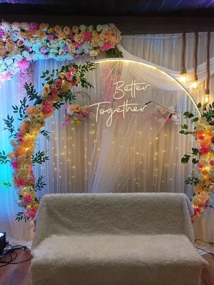 A popular choice for modern engagements, this setup includes a circular floral arch with multi-colored flowers, a "Better Together" neon sign, and hanging bulbs. It's a vibrant and romantic backdrop for any celebration.