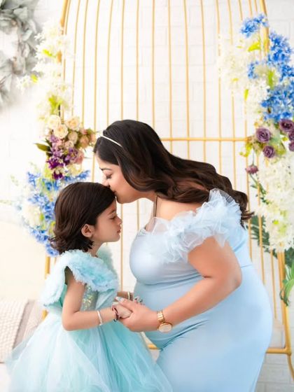 A precious moment between a mother and her daughter. A gentle kiss on the forehead is a promise of love, as they both anticipate the arrival of the newest family member. The matching blue dresses are a sweet touch.