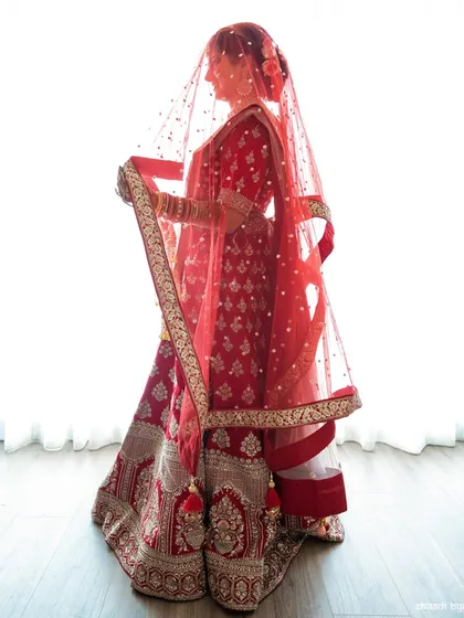 A classic bridal portrait against a bright window, creating a beautiful silhouette effect with her red veil.
