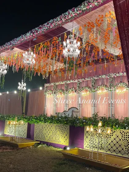 A vibrant and colorful stage with hanging orange and green florals, set against a backdrop of intricate latticework.