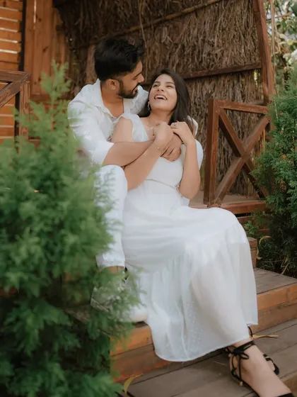 A moment of pure, uninhibited laughter on a rustic wooden porch. Dressed in coordinated white, this couple's joy is infectious, showcasing a perfectly candid moment from their pre-wedding shoot.