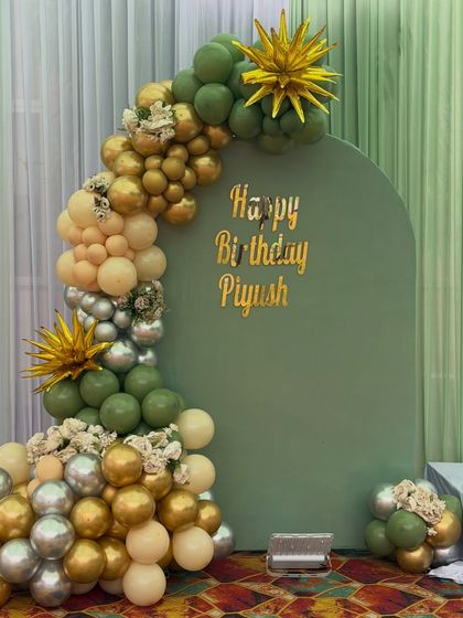 A stylish birthday backdrop for Piyush. The olive green arch is paired with a sophisticated balloon arrangement in shades of green, gold, silver, and beige.