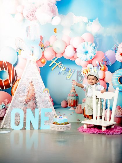 Every first birthday deserves a grand celebration. This little boy looks absolutely regal in his party hat, standing by his cake in a beautifully decorated studio setting.