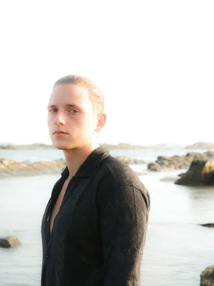 An outdoor portrait session by the sea. The overexposed background and the subject's direct gaze create a serene yet powerful mood.
