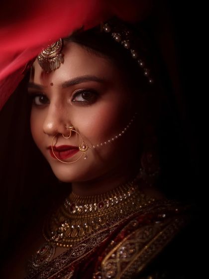 A dramatic and beautiful bridal portrait. The red veil and dark background make her features and gold jewelry pop.