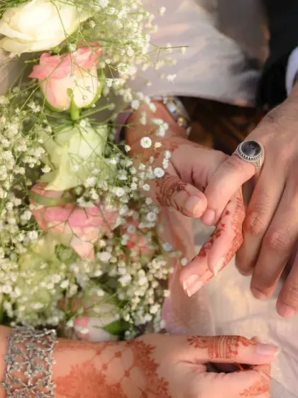 A close-up of the couple's hands during their engagement ceremony. This shot focuses on the tender connection and the promise of forever, with the bride's henna and bouquet adding beautiful detail.