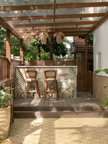 This outdoor bar and patio at the Verdant Manor was designed as a tropical reverie. The bar is clad in botanical tiles and paired with classic cane and wood bar stools, all under a glass and wood pergola.