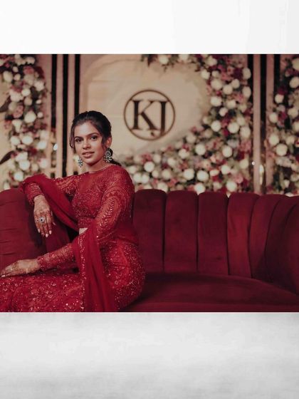 A wide shot of the bride in a vibrant red lehenga, seated on a red sofa against a floral backdrop.