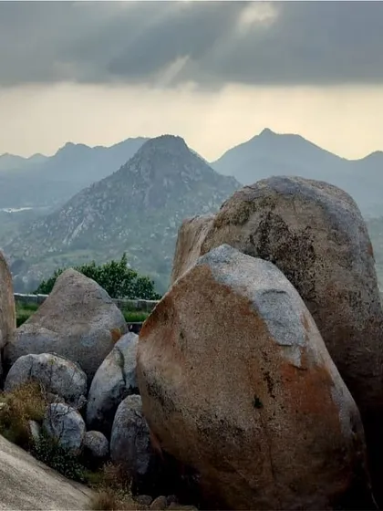 A lone trekker stands on a boulder, taking in the vast, rocky landscape near Gudibande fort.