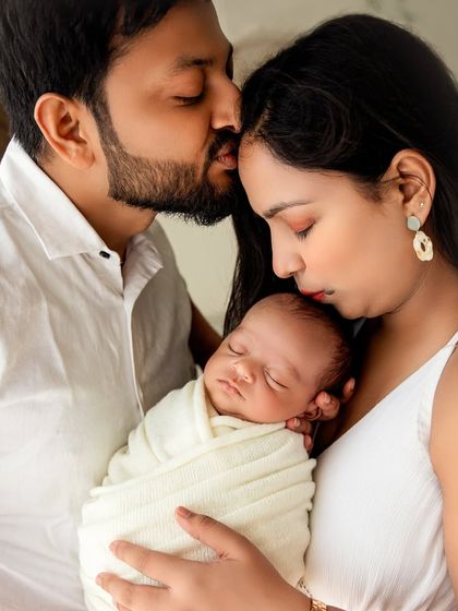A tender moment of the family huddling close, with both parents kissing and holding their newborn.