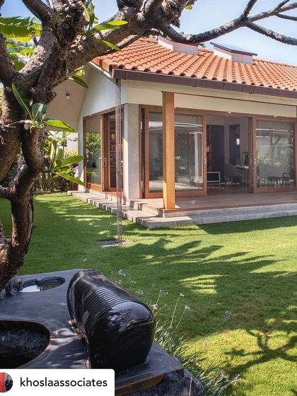 A view across a manicured lawn towards a modern villa, with a custom stone music bench in the foreground. The landscape is designed with clean lines and open spaces, creating a sensory experience that connects with the home's architecture.