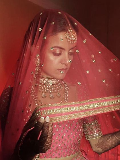 An artistic shot of a bride under her sheer red veil. The delicate embroidery of the dupatta frames her face, highlighting the soft eyeshadow and intricate henna design.
