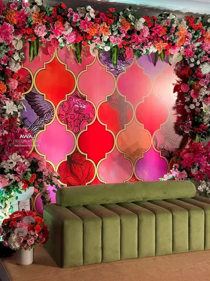 A vibrant Mehendi seating area with a colorful patterned backdrop, framed by a cascade of multi-colored flowers.