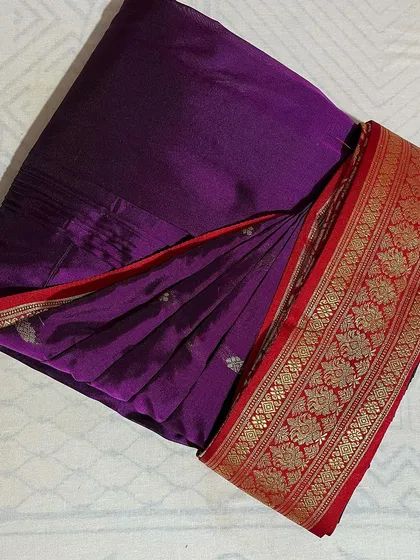 A deep purple saree with a striking red and gold border, folded to perfection.