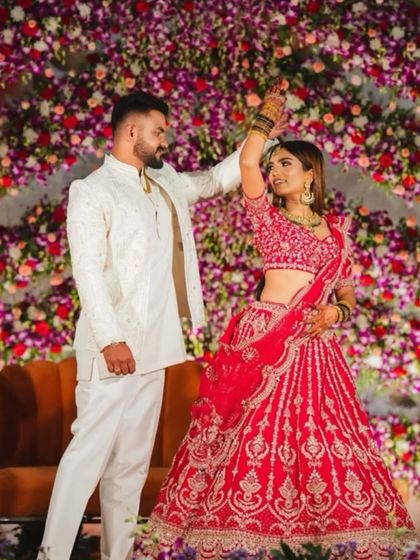 A candid moment of a couple dancing at their reception. The backdrop is a stunning wall of purple and pink orchids, adding to the festive and romantic mood.