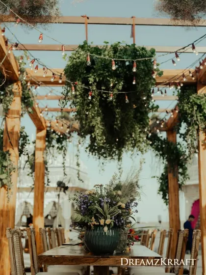 A rustic yet elegant dining setup under a wooden pergola with hanging greenery. This design is perfect for creating a warm, communal atmosphere for a welcome dinner or brunch.