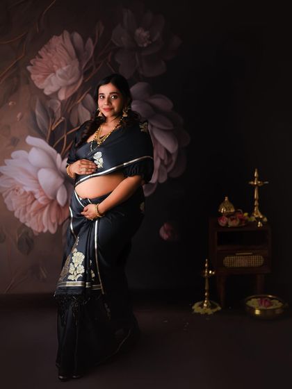 Draped in an elegant black saree, this mother-to-be stands proudly in a studio setting designed to feel both traditional and artistic. This was her first maternity shoot, and she was absolutely radiant.