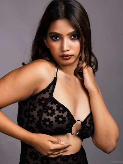 A close-up portrait of a model in a sheer black floral dress, with a sultry and confident look.