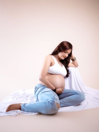 A moment of quiet, a lifetime of love growing within. This serene portrait in jeans and a white top beautifully reflects the calm, joy, and wonder of motherhood.