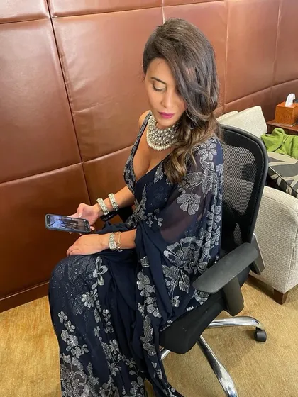 A full view of a sophisticated party look. The side-swept hair and glamorous makeup were designed to complement her elegant navy blue and silver saree.
